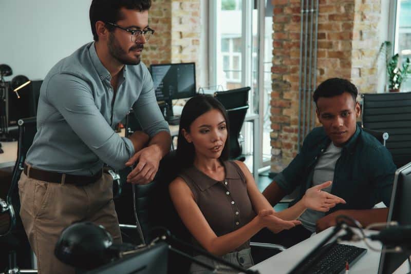 Três profissionais em frente ao computador olham para o monitor e traçam estratégias para implementar a Contabilidade 4.0.