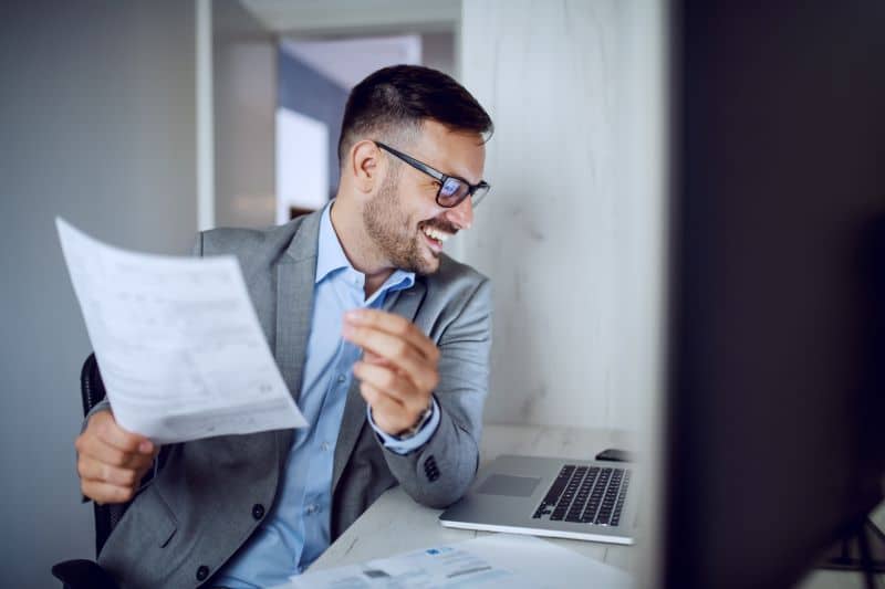 Contador sorridente usando computador para validar nota fiscal em suas mãos.