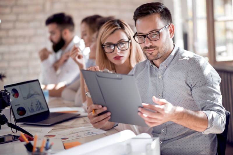 Mulher e homem analisando o que é ARPU enquanto colegas trabalham ao fundo no escritório.