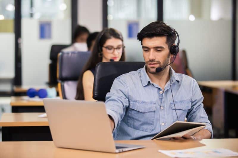 Atendente no computador com headset entrando em contato para transmitir mensagem de cobrança para clientes.