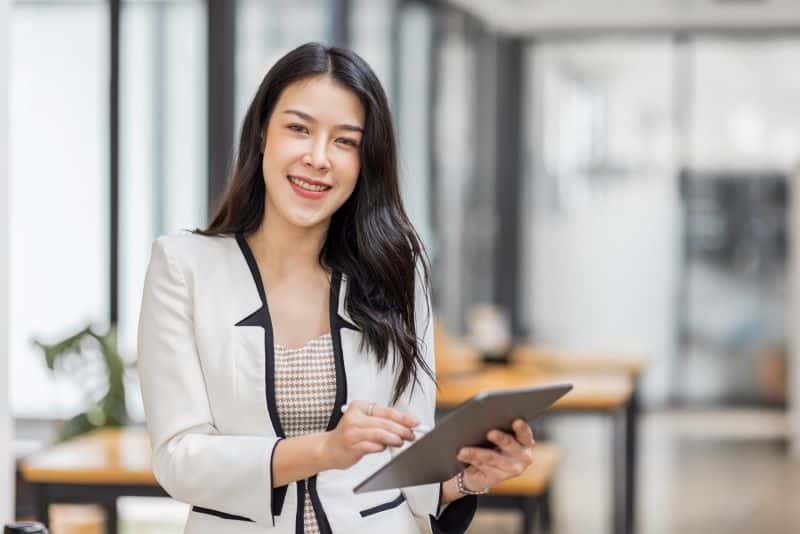 Mulher sorridente em escritório despreocupada com software no tablet que a ajuda a calcular IPCA acumulado.