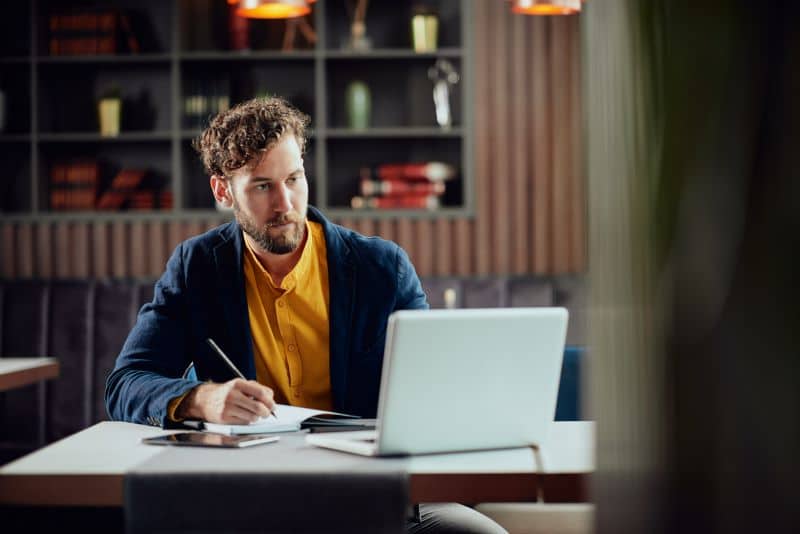 Cohort o que é: homem realizando análise no computador e fazendo anotações em agenda.