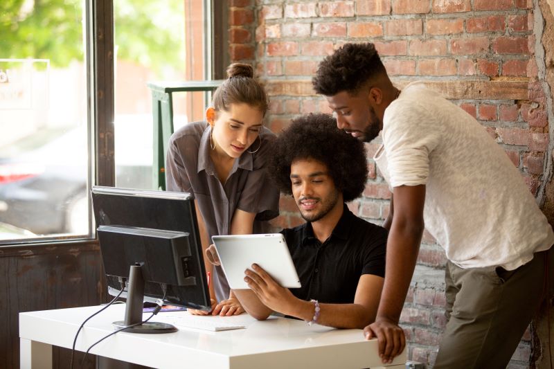 Sistema de gestão integrada: três colegas usando tablet em volta de mesa no escritório.