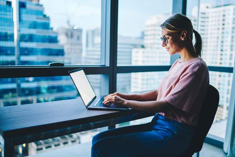 ferramentas para controle orçamentário: mulher trabalhando em notebook em escritório com vista para prédios na rua