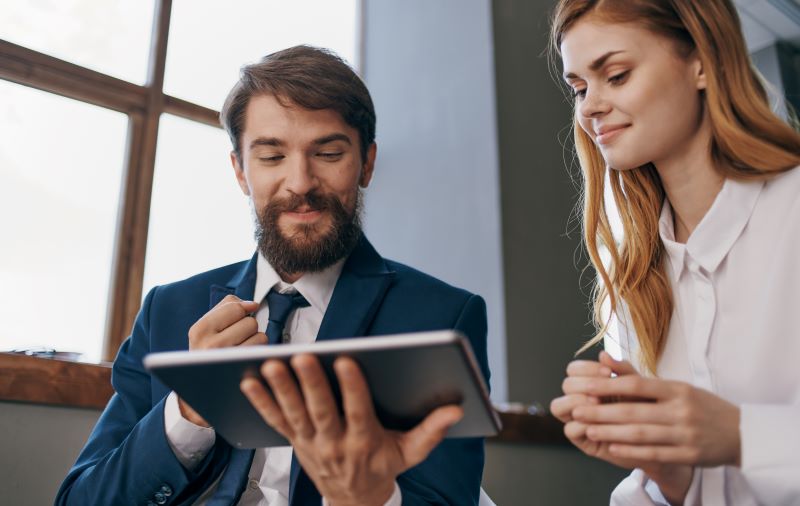 csll lucro presumido​: homem e mulher em escritório analisando documentos em tablet