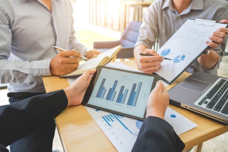 estatística descritiva​: três homens analisando gráficos e falando sobre gestão financeira